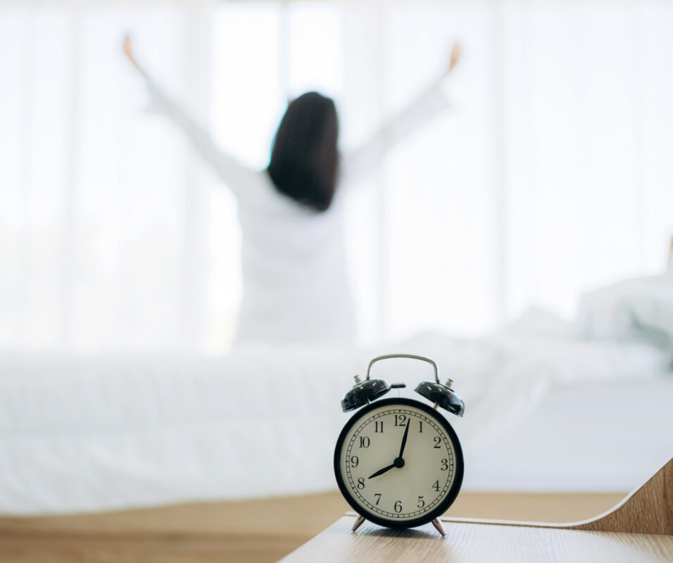 A person stretching in the morning in the background, with a clock in the foreground, symbolizing the importance of time in building daily routines for mental health and personal growth.