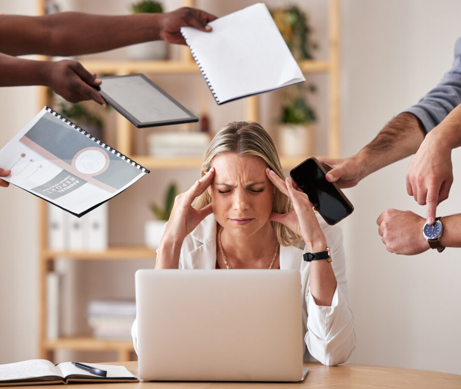 A stressed businesswoman sits at her desk with her head in her hands, surrounded by paperwork and her phone, symbolizing burnout and workplace stress.