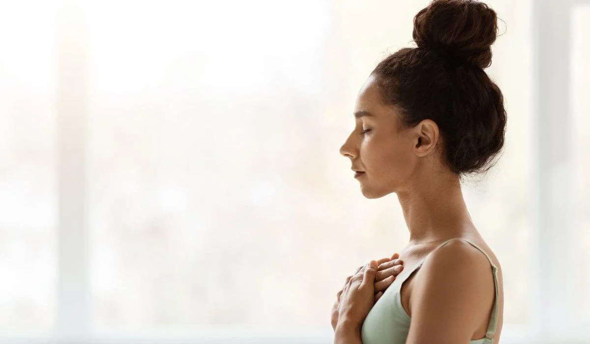 A serene woman embracing heart power, with her hands placed gently on her heart and eyes closed in meditation.